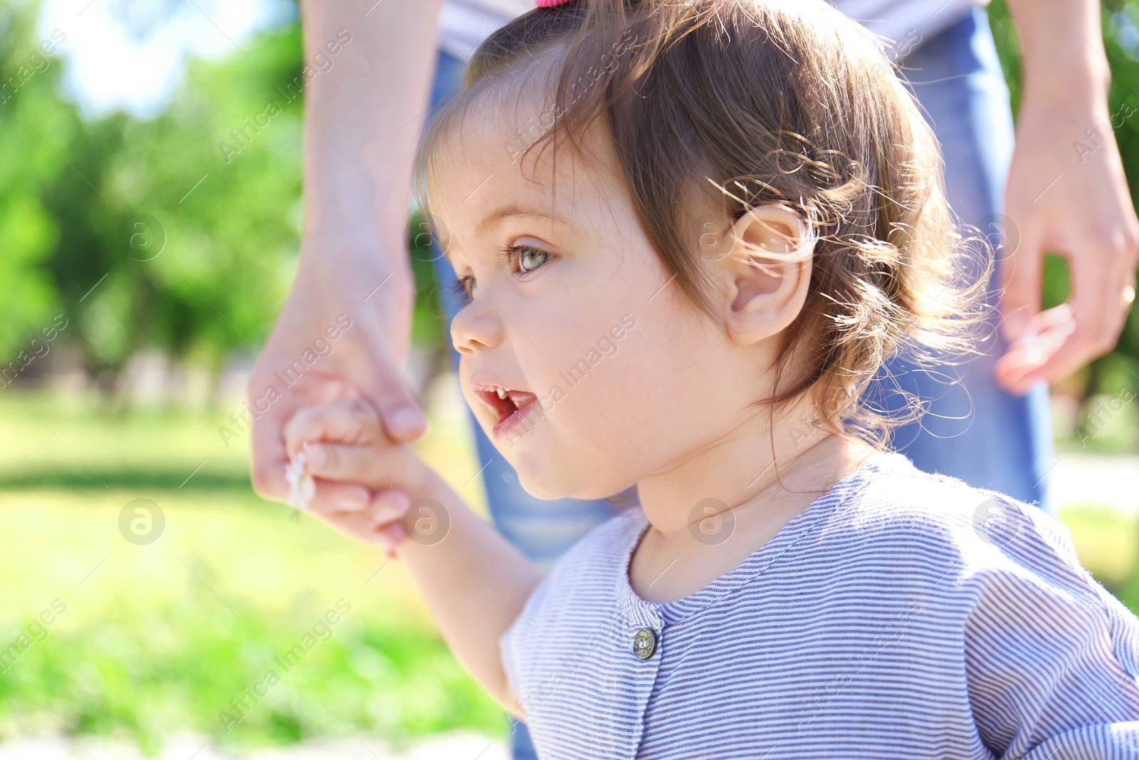 Photo of Adorable baby girl holding mother's hand while learning to walk outdoors