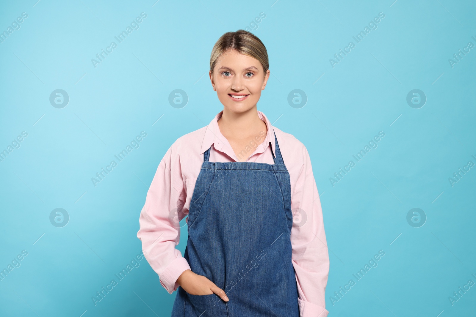 Photo of Beautiful young woman in denim apron on light blue background