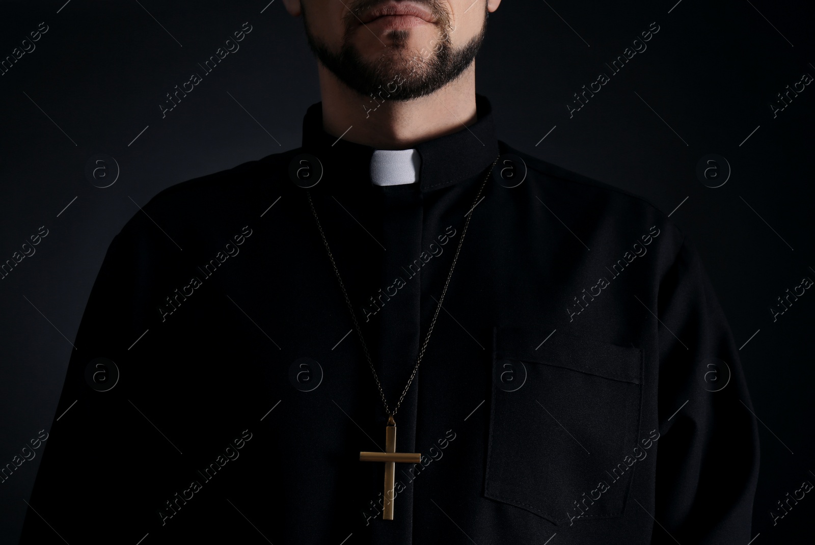 Photo of Priest wearing cassock with clerical collar on dark background, closeup