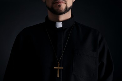 Photo of Priest wearing cassock with clerical collar on dark background, closeup
