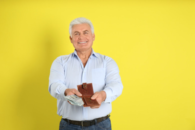 Photo of Happy senior man with cash money and wallet on yellow background. Space for text