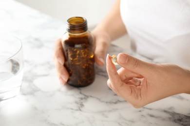 Photo of Woman with fish oil pills at table, closeup