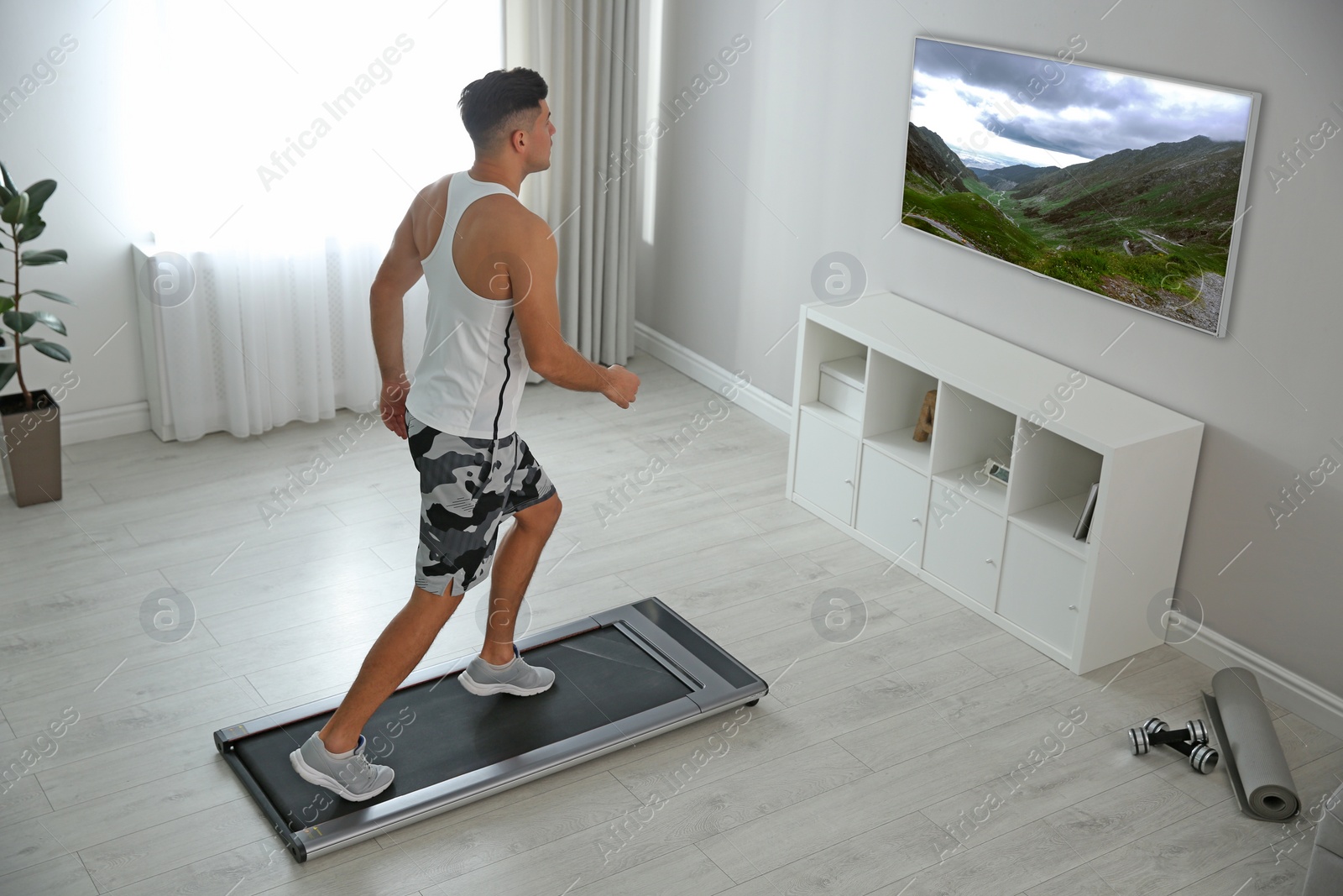 Image of Sporty man training on walking treadmill and watching TV at home
