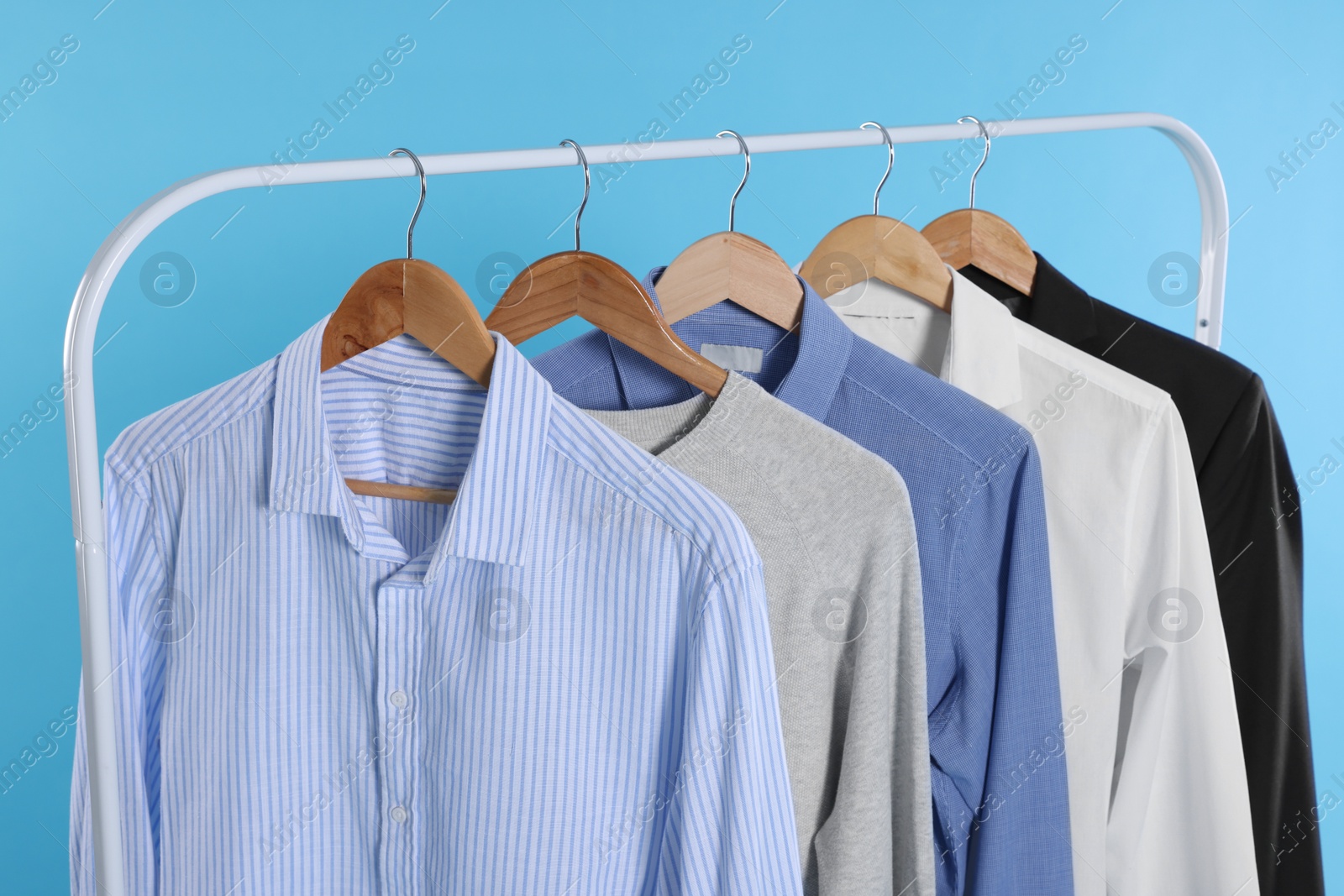 Photo of Rack with stylish clothes on wooden hangers against light blue background