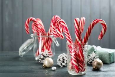 Photo of Many sweet candy canes, gift boxes and Christmas decor on grey wooden table. Space for text