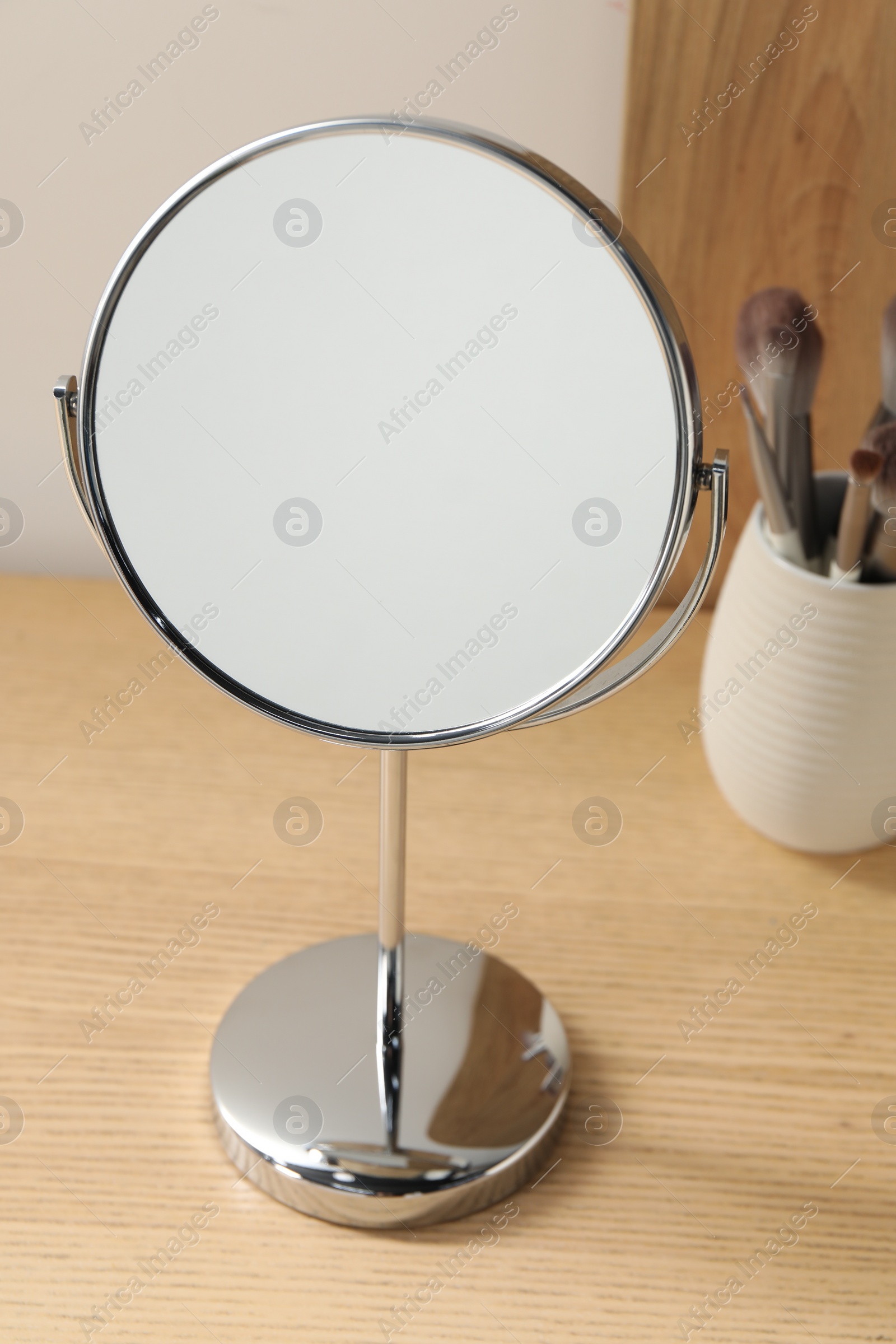 Photo of Mirror and makeup brushes on wooden dressing table, closeup