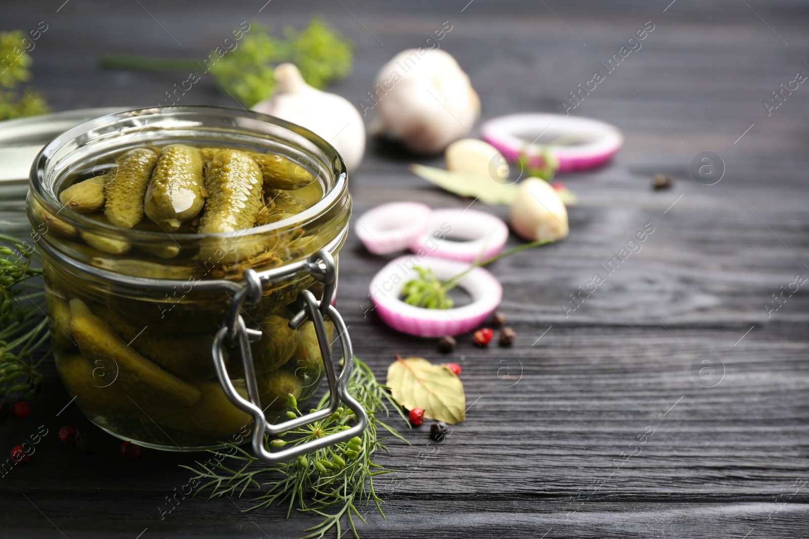 Photo of Glass jar of pickled cucumbers on black wooden table. Space for text