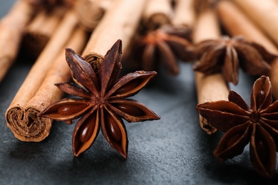 Photo of Aromatic cinnamon sticks and anise on black table, closeup