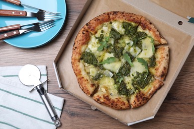 Delicious pizza with pesto, cheese and arugula in cardboard box served on wooden table, flat lay