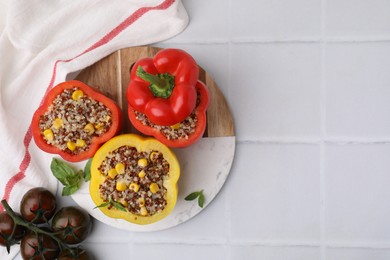 Photo of Quinoa stuffed bell peppers, tomatoes and basil on white tiled table, flat lay. Space for text