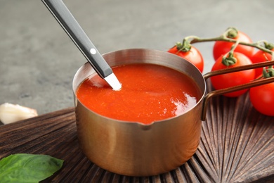 Photo of Pan with tomato sauce and spoon on wooden board, closeup