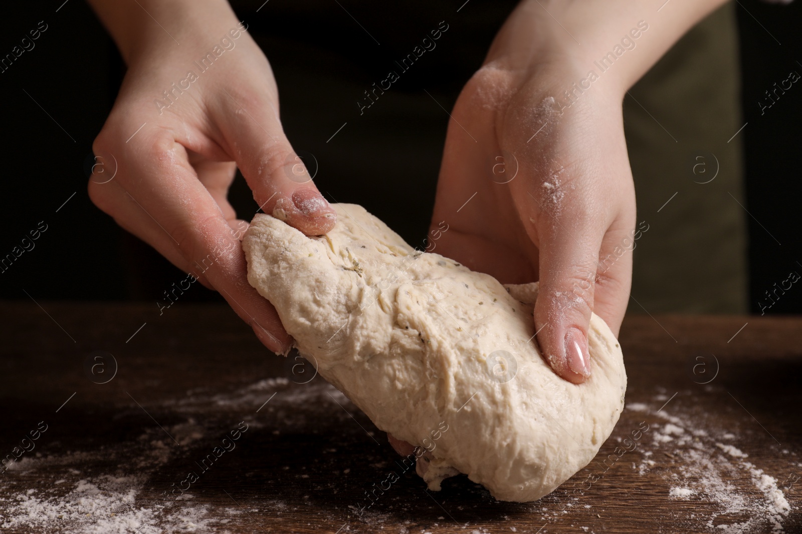 Photo of Woman kneading dough at wooden table, closeup. Cooking traditional grissini