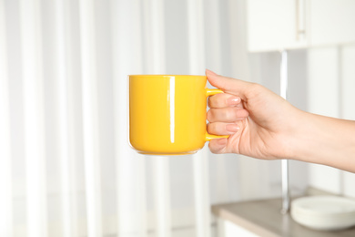 Woman holding yellow cup at home, closeup