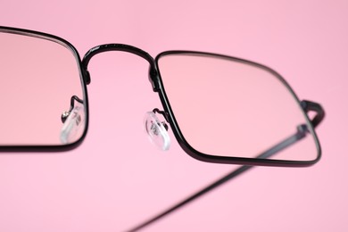 Stylish pair of glasses with black frame on pink background, closeup