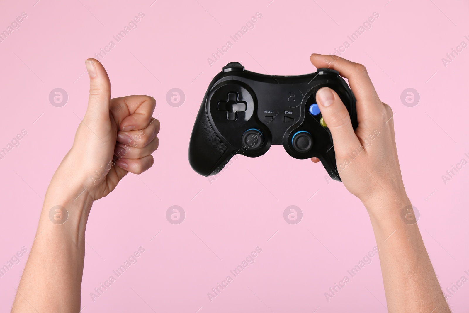 Photo of Woman with game controller showing thumbs up on pink background, closeup