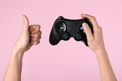 Woman with game controller showing thumbs up on pink background, closeup