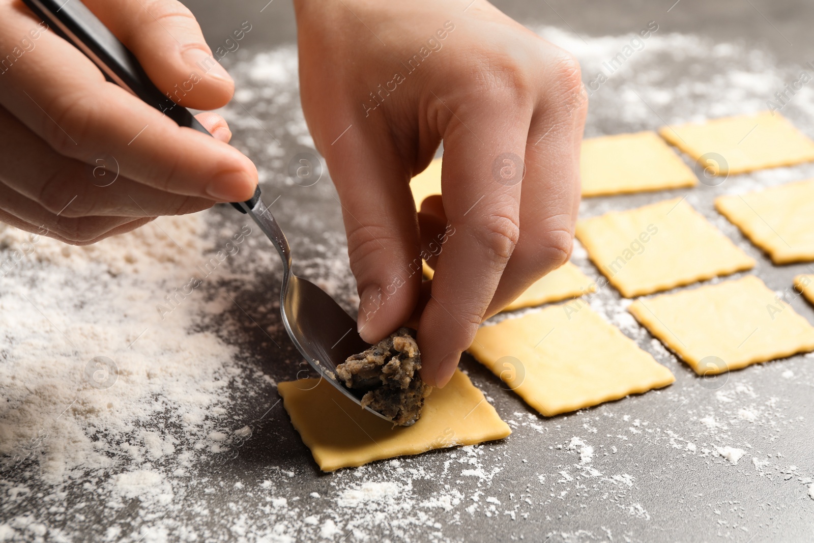 Photo of Woman making ravioli at grey table, closeup. Italian pasta