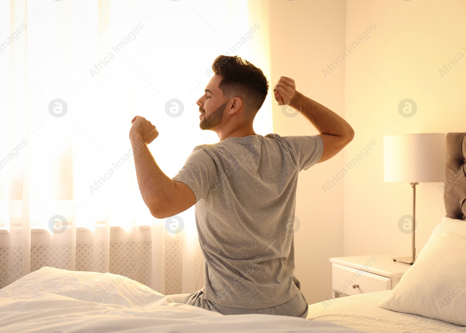 Photo of Young man stretching on bed at home. Lazy morning