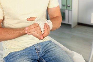 Man with hand wrapped in medical bandage at hospital, closeup. Space for text