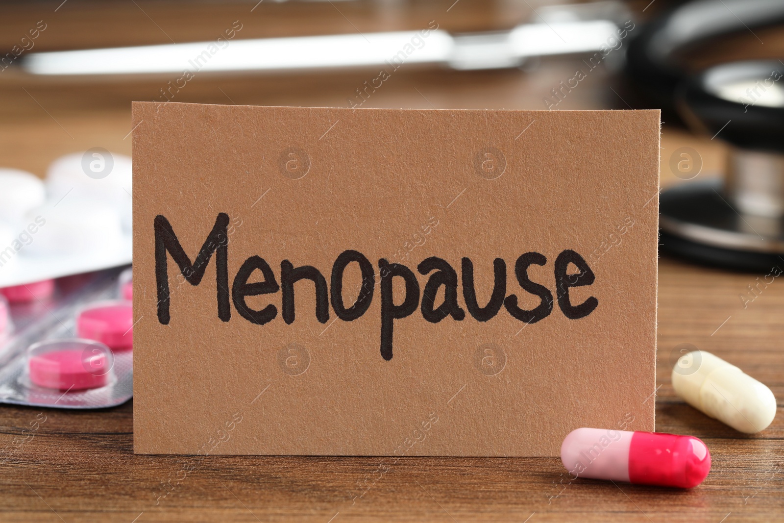 Photo of Card with word Menopause and pills on wooden table, closeup