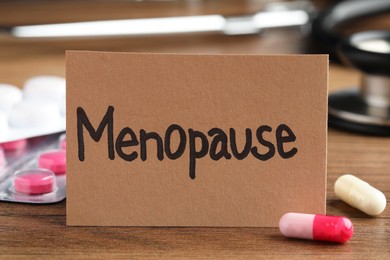 Card with word Menopause and pills on wooden table, closeup