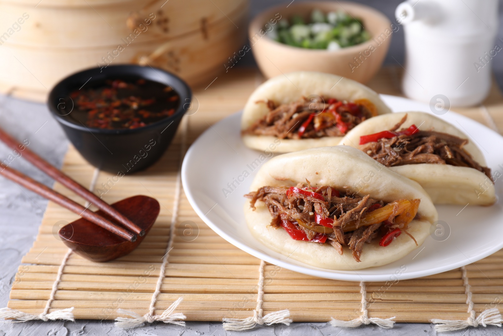 Photo of Delicious gua bao (pork belly buns), chopsticks and sauce on grey textured table, closeup