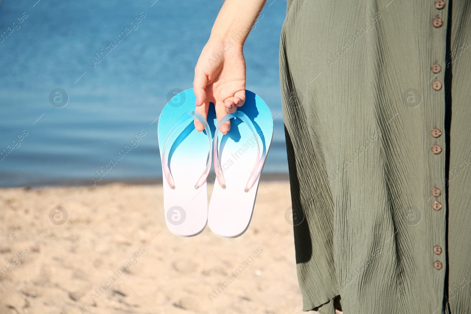 Photo of Woman holding flip-flops on beach, closeup. Space for text