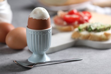 Photo of Tasty boiled egg in cup served on light grey table, closeup
