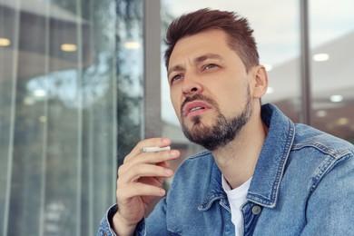 Photo of Handsome man smoking cigarette outdoors. Space for text