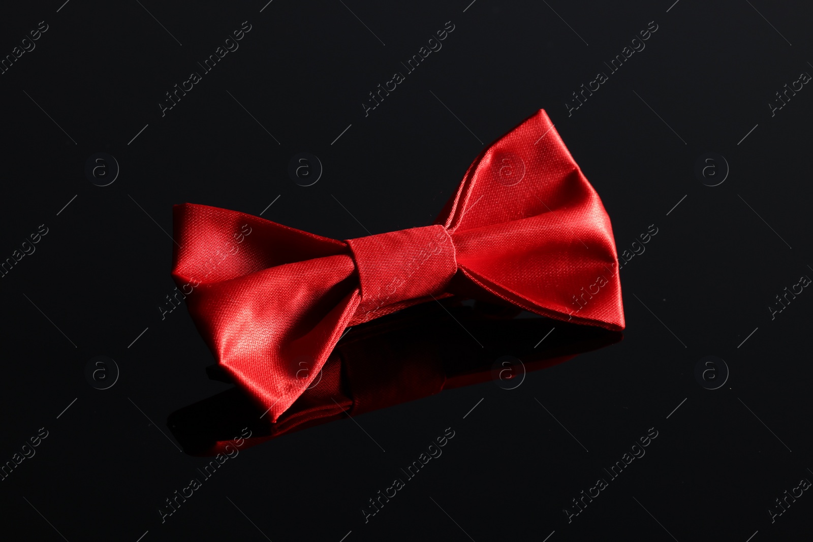 Photo of Stylish red bow tie on black mirror surface