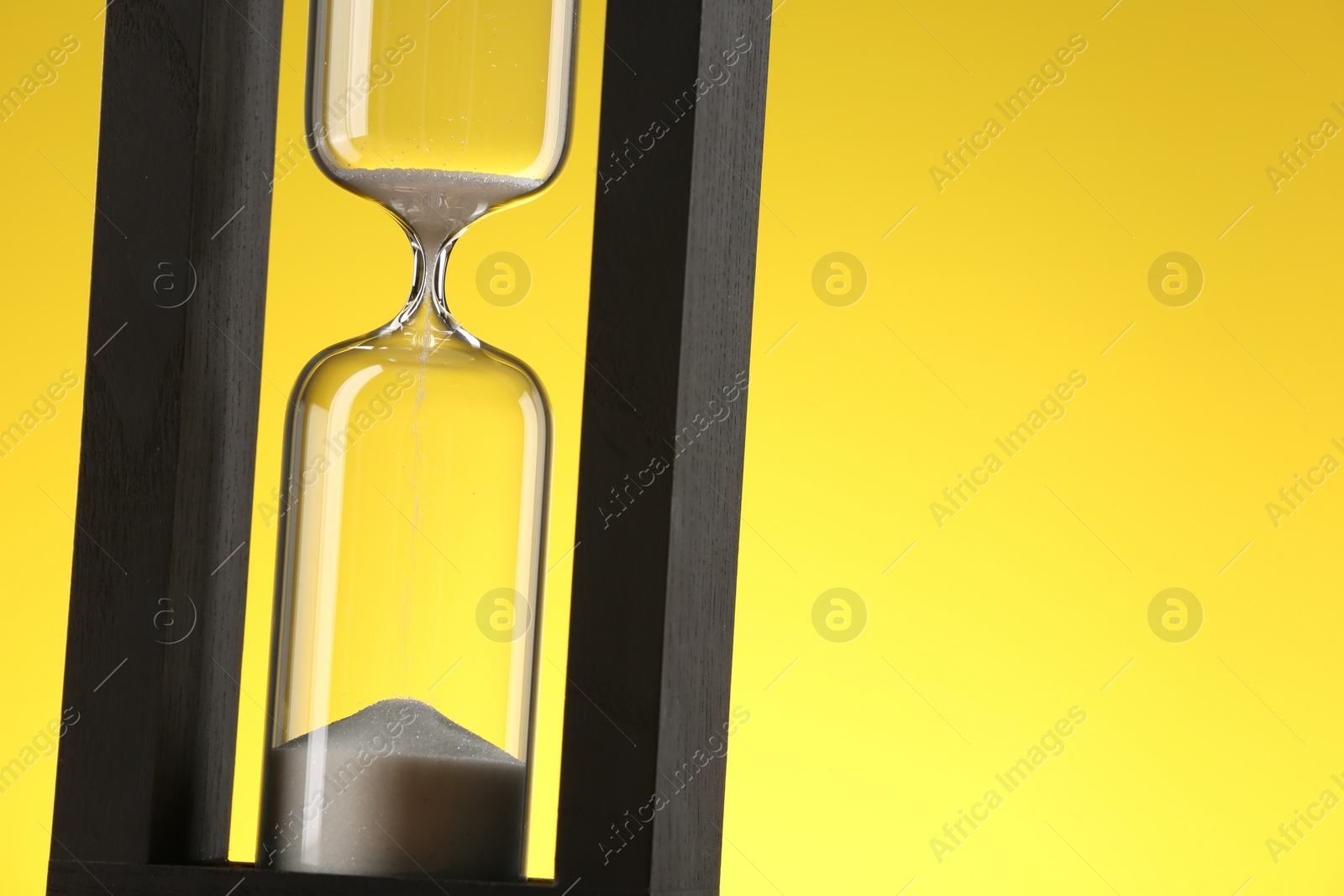 Photo of Hourglass with flowing sand against yellow background, closeup. Space for text