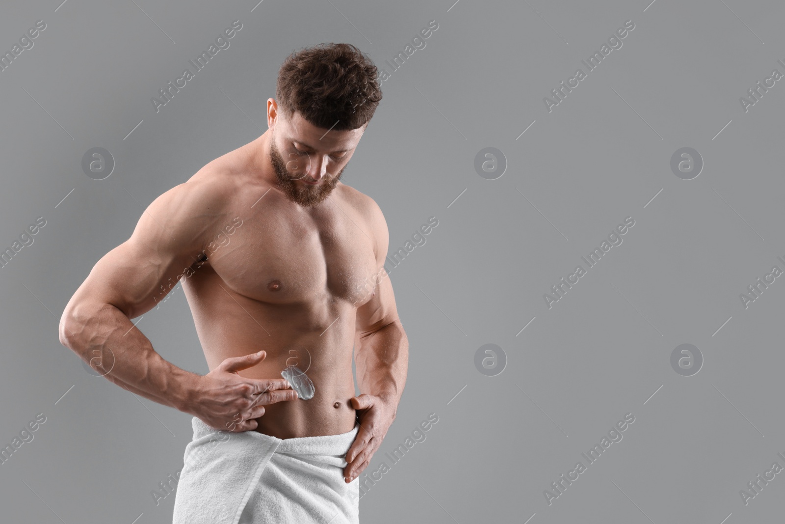 Photo of Handsome man applying moisturizing cream onto his body on grey background, space for text