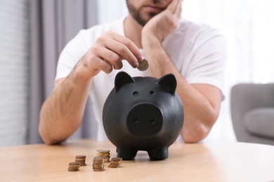 Photo of Sad young man with piggy bank saving money at home, closeup
