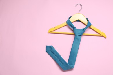 Hanger with blue necktie on pink background, top view. Space for text