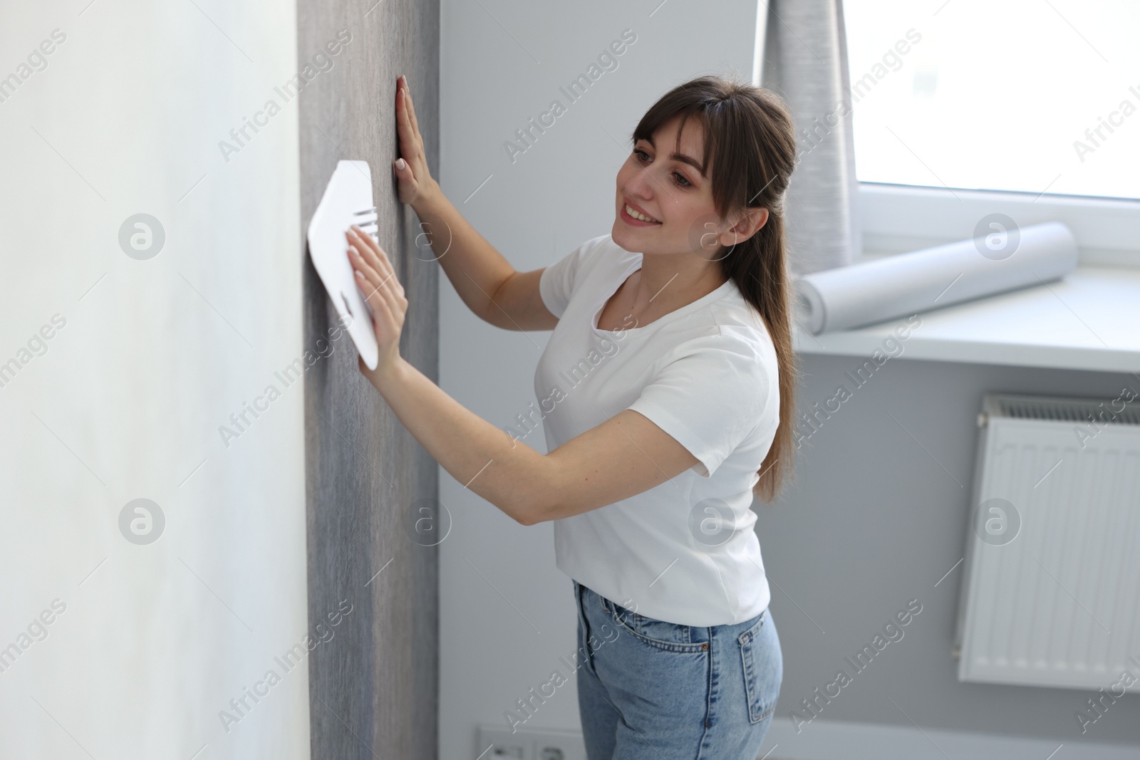 Photo of Woman smoothing stylish gray wallpaper in room