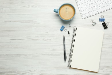 Photo of Blank notebook, cup of coffee, computer keyboard and office stationery on white wooden table, flat lay. Space for text