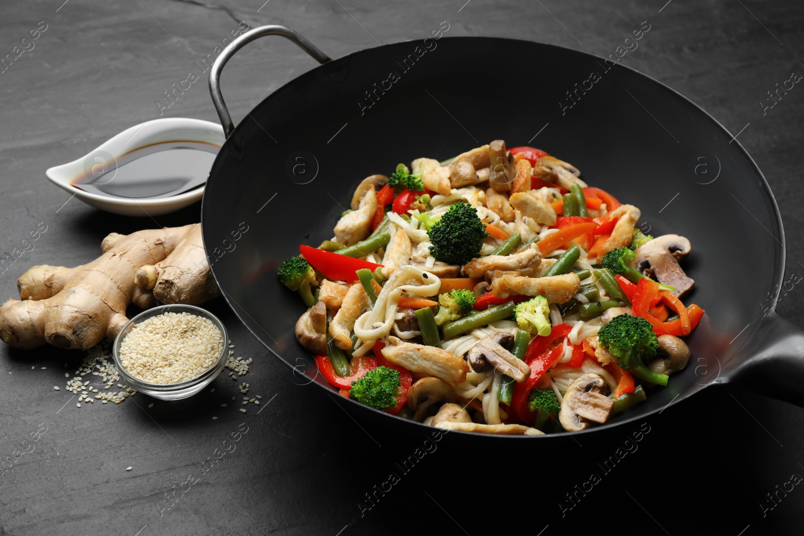 Photo of Stir fried noodles with mushrooms, chicken and vegetables in wok on black table