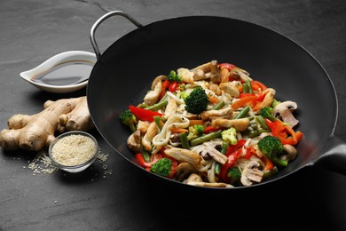 Stir fried noodles with mushrooms, chicken and vegetables in wok on black table