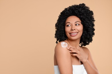 Photo of Young woman applying body cream onto shoulder on beige background. Space for text