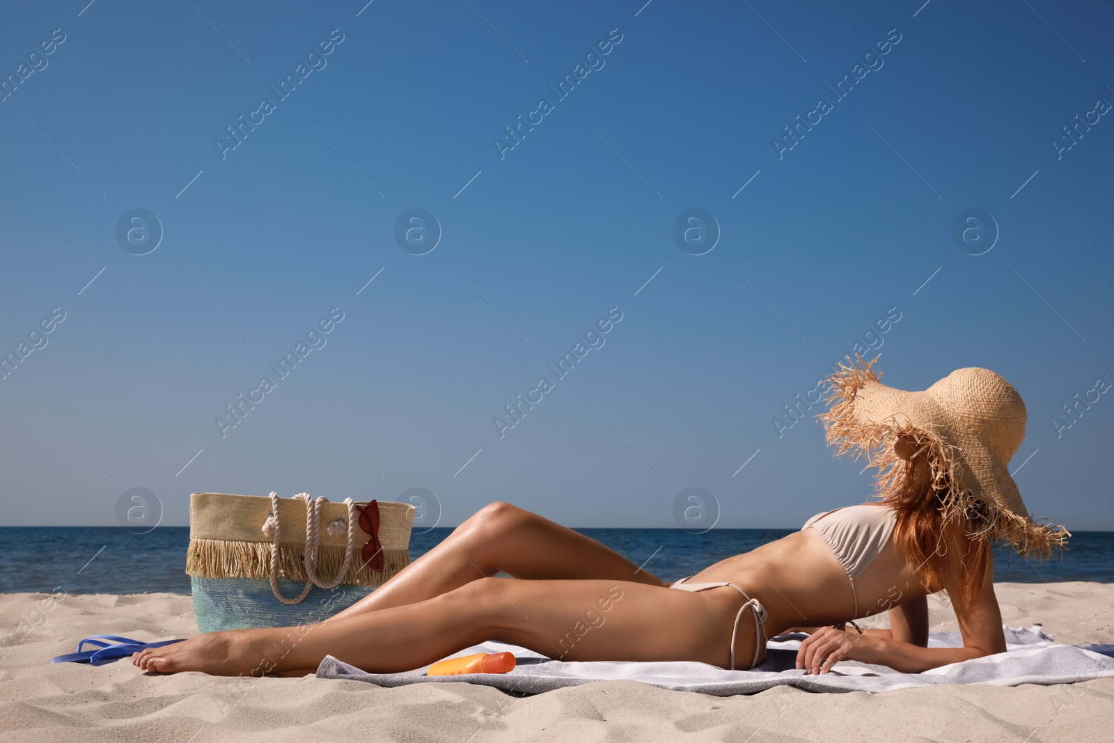 Photo of Woman with beach bag and straw hat on sand near sea