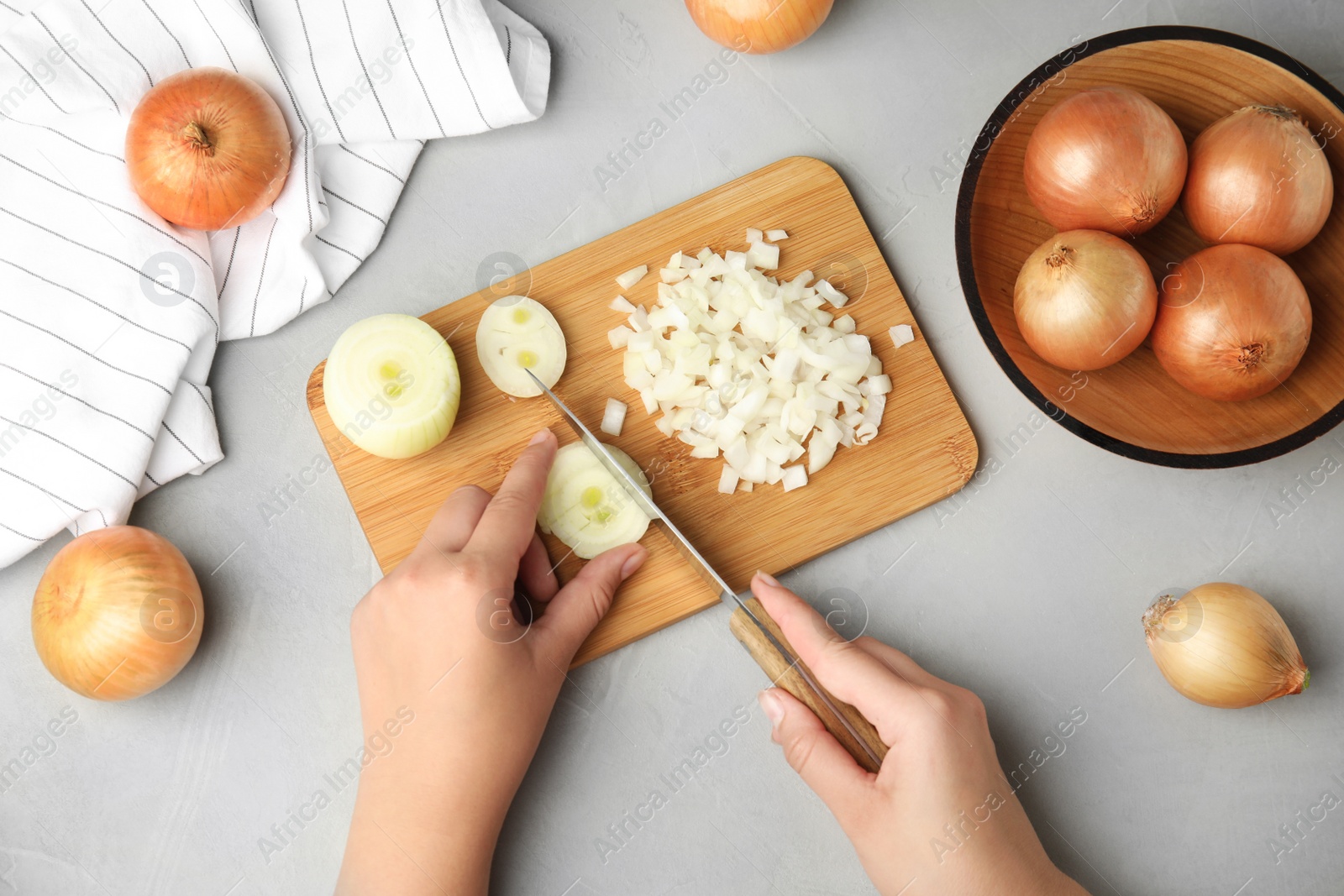 Photo of Woman cutting ripe onion on wooden board at grey table, top view