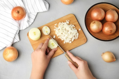 Photo of Woman cutting ripe onion on wooden board at grey table, top view
