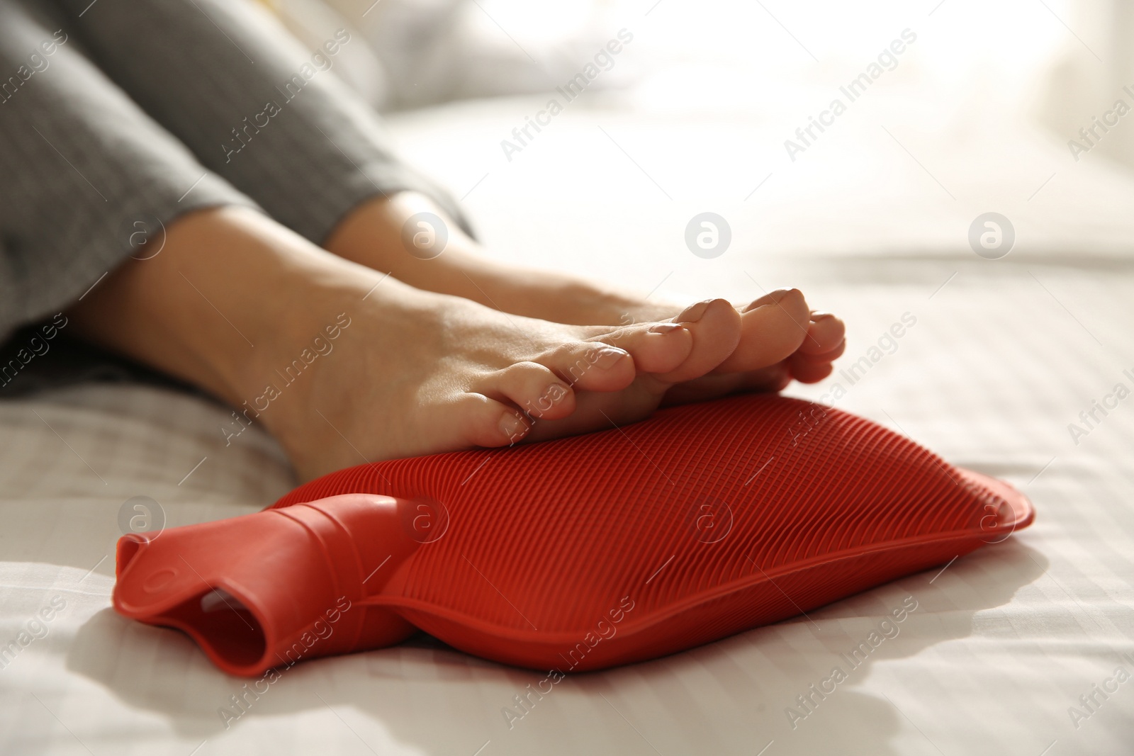 Photo of Woman warming feet with hot water bottle on bed, closeup