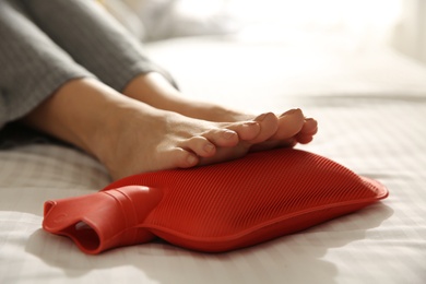 Woman warming feet with hot water bottle on bed, closeup