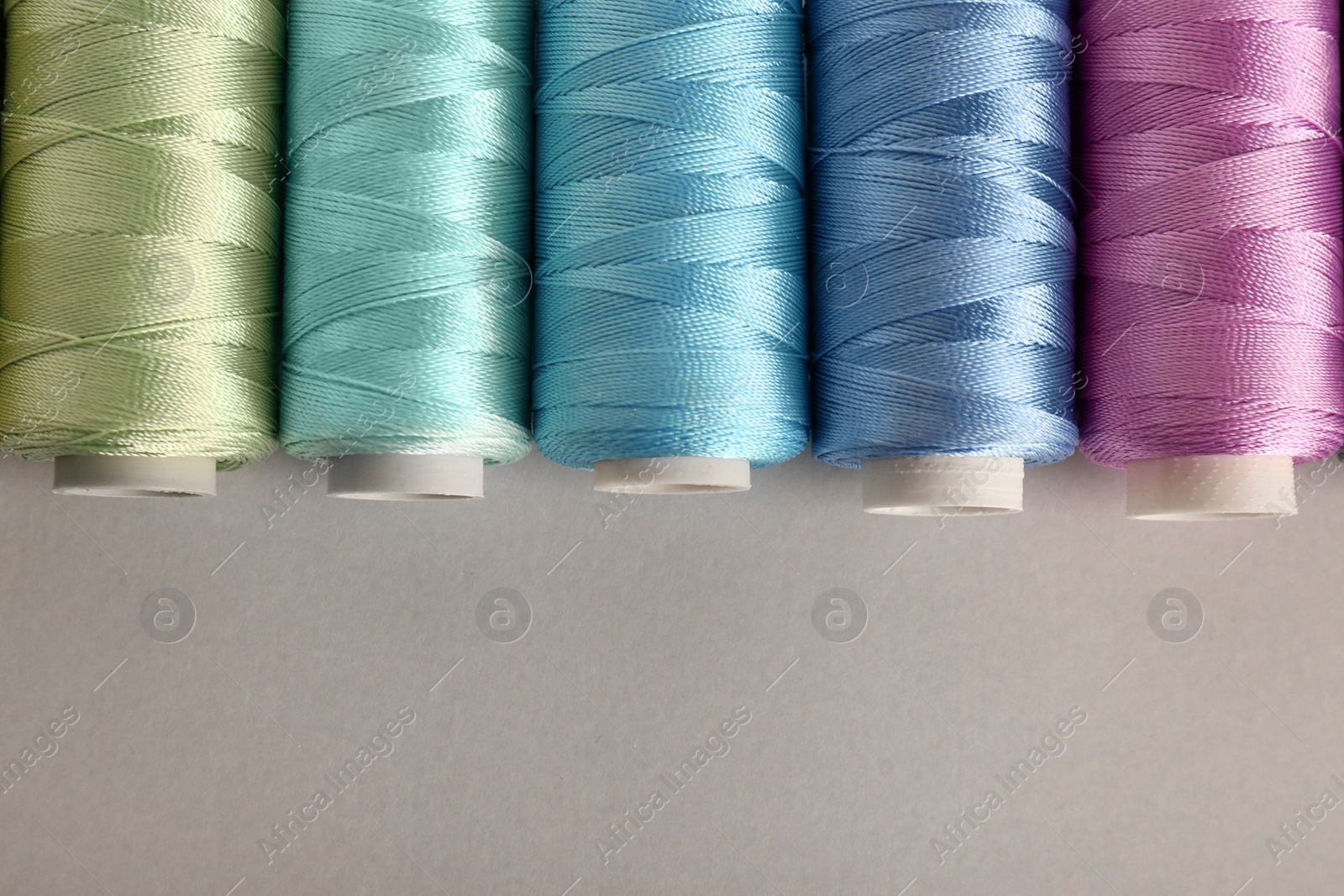 Photo of Different colorful sewing threads on light grey background, flat lay. Space for text