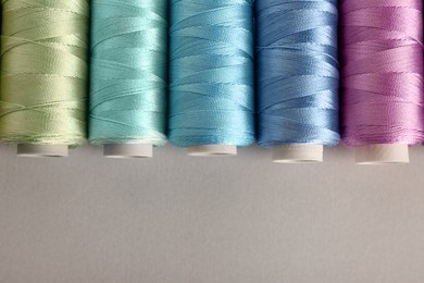 Photo of Different colorful sewing threads on light grey background, flat lay. Space for text