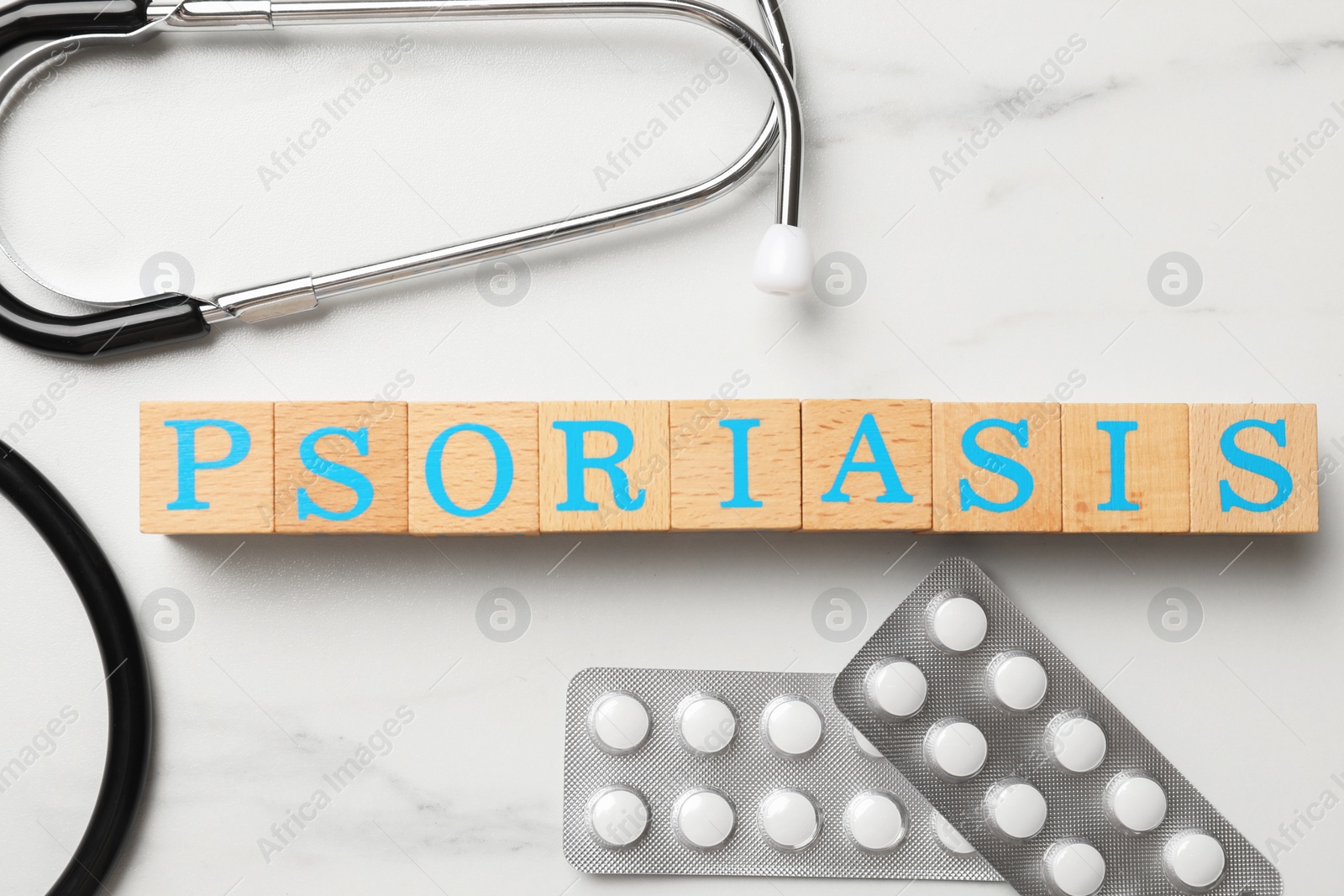 Photo of Word Psoriasis made of wooden cubes with letters, stethoscope and pills on white marble table, flat lay