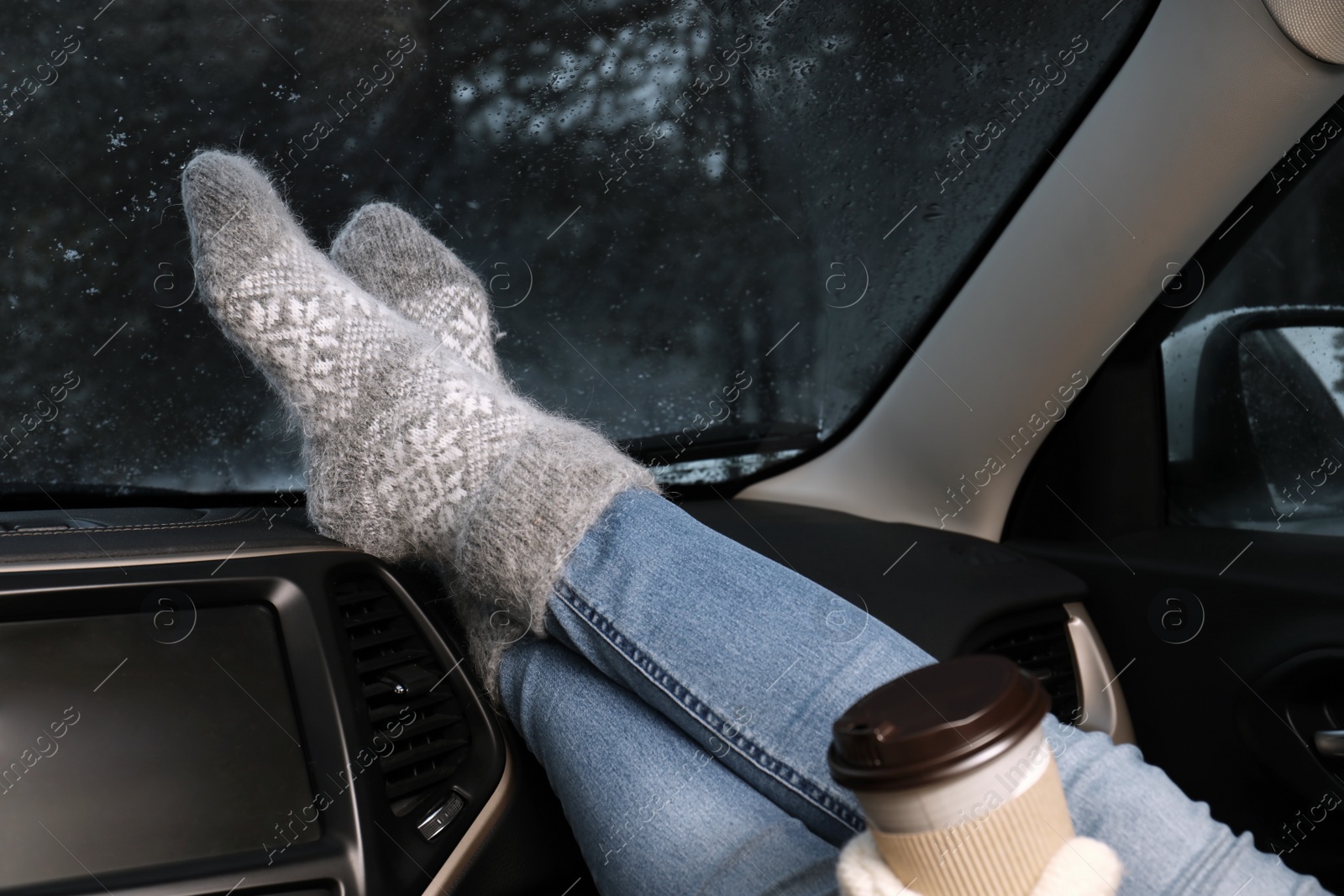 Photo of Woman in warm socks with coffee resting inside car, closeup