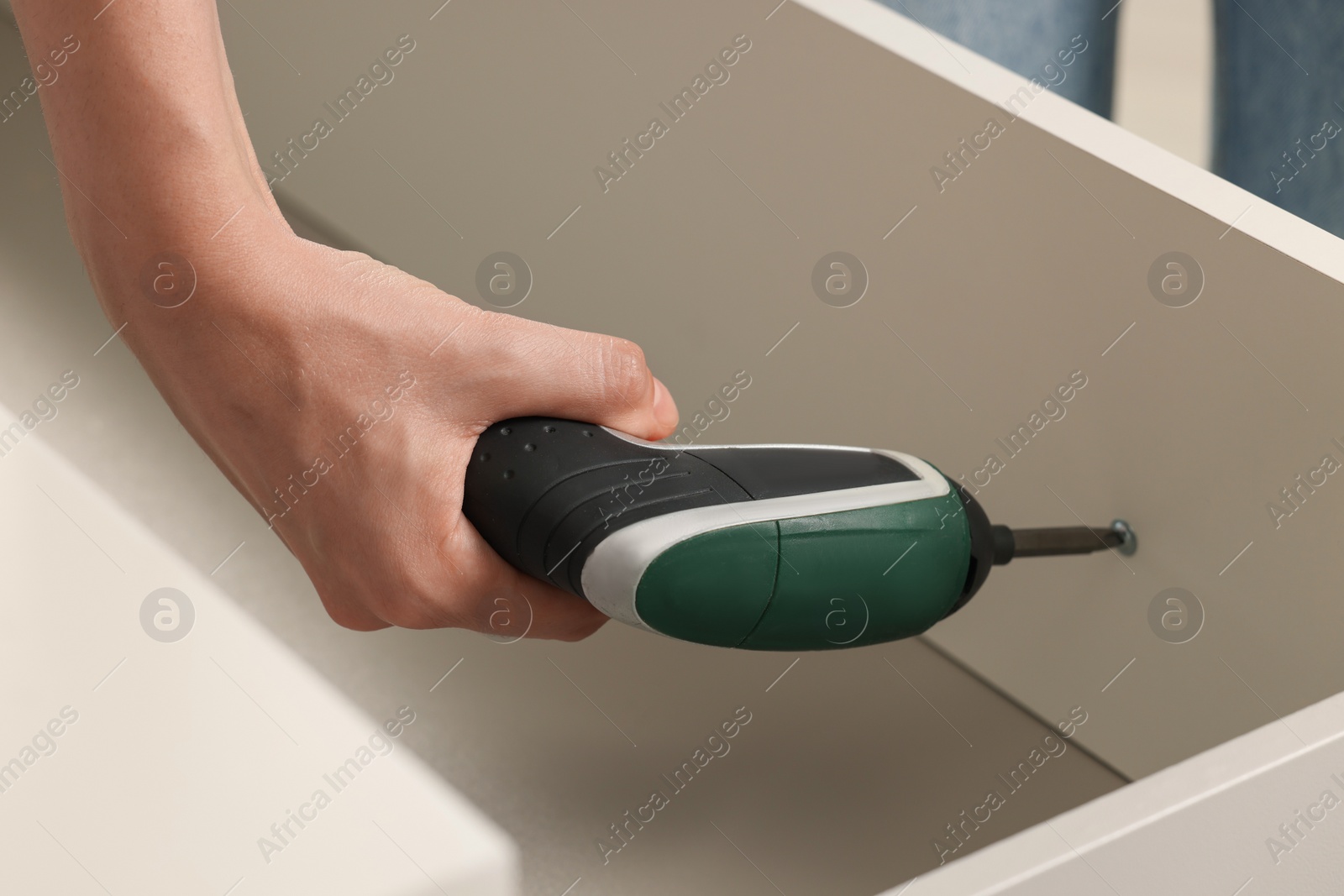 Photo of Woman with electric screwdriver assembling drawer, closeup