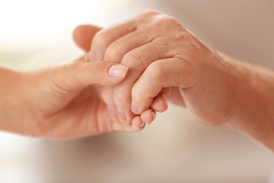 Photo of Young woman holding elderly man hand on blurred background, closeup. Help service